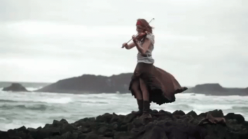 a woman with a violin standing on rocks near the ocean