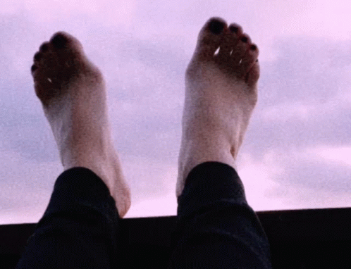 a person standing at a window with his feet propped up on the window sill