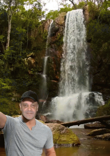 a man poses in front of the waterfall
