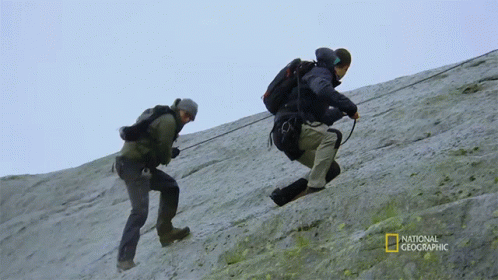 two people are climbing up a steep hill