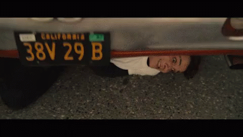 a young man under a car with his head under the license plate