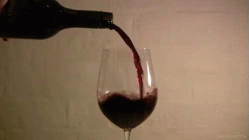 a glass is filled with red wine as it's poured