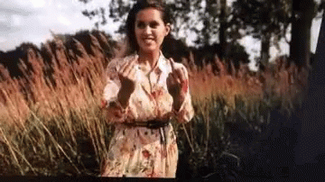 woman standing in the grass with her hands out to her face