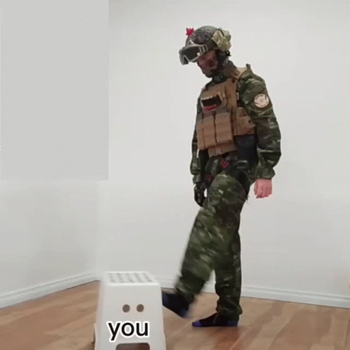 a man in fatigues standing in a room with a you sign in front of him