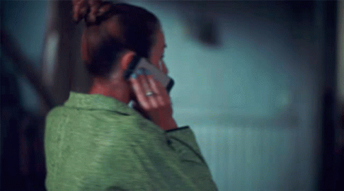 a woman wearing a green shirt holding a cell phone to her ear
