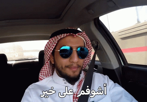 man wearing arabic garb driving in car with words above him