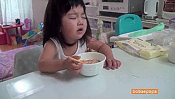 a child crying while holding a bowl of cereal