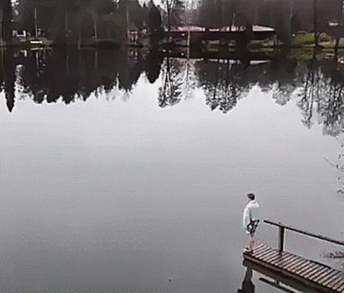 the man in white shirt is standing on the dock near a lake