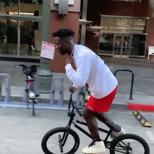 a black man wearing an orange shirt is riding a bicycle