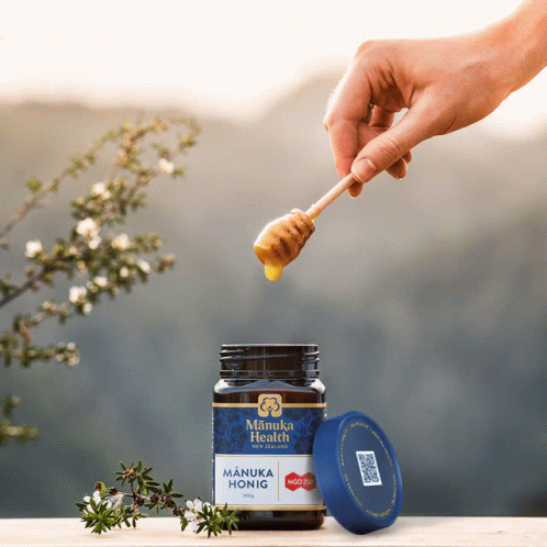 a jar of manuka honuig is being dipped with a toothbrush by someone in blue