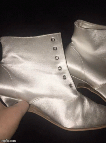 someone's hand reaching for the heel of a shiny ankle high boot