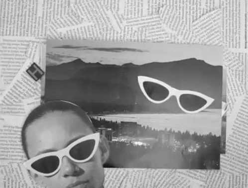 a woman in white sunglasses laying down with mountains and trees above her