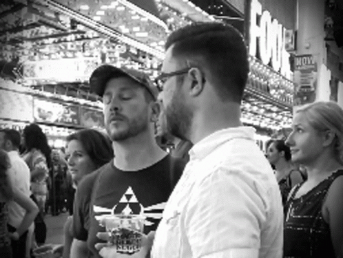 a man in glasses is standing around drinking and listening to another person