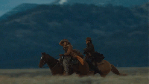 two men ride horses near a mountain
