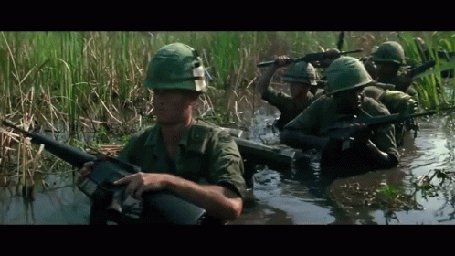 the military is traveling through a stream and are wearing helmets