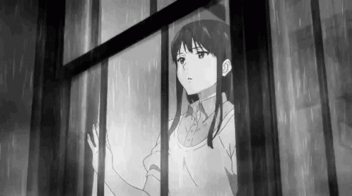 a woman stands looking out the window and is in the rain