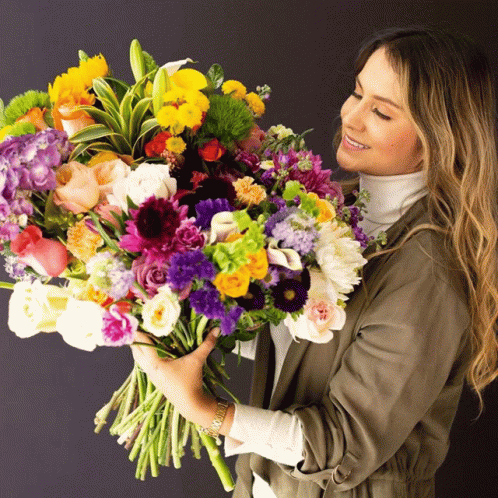 a woman is holding a colorful bouquet of flowers