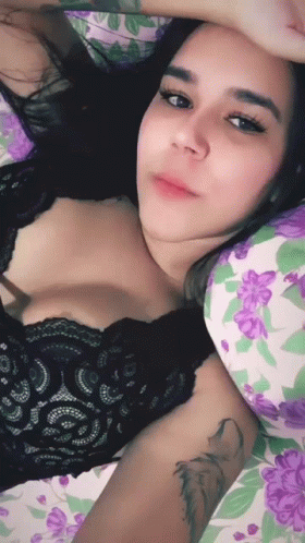 a women in black lacy top and floral outfit lying down on bed