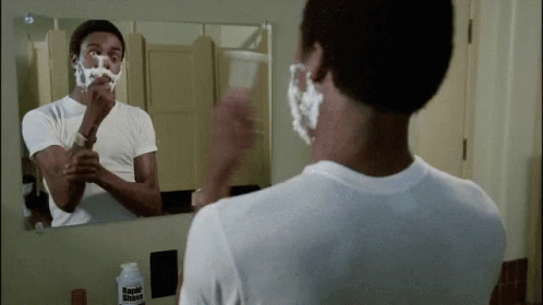 man shaving his teeth in the bathroom mirror