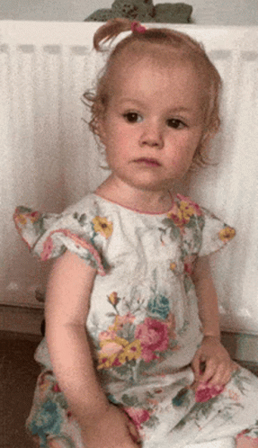 an infant sits on a step, wearing a dress with flowers