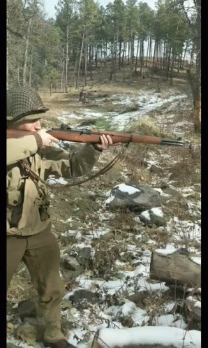 man standing in the woods with his rifle and looking up