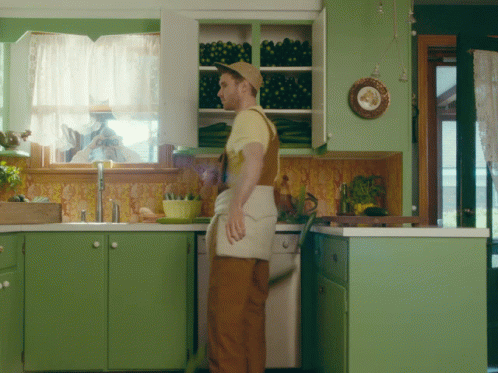 the man is standing in his green kitchen