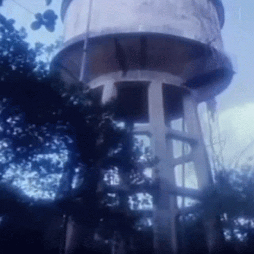 a tall white water tower sitting next to a lush green tree