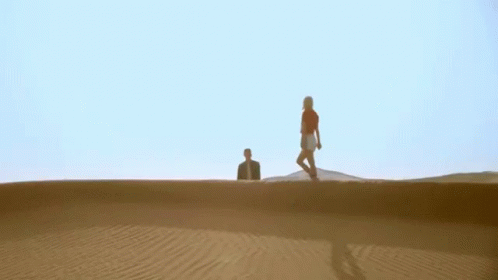 three people walking across a large sand hill
