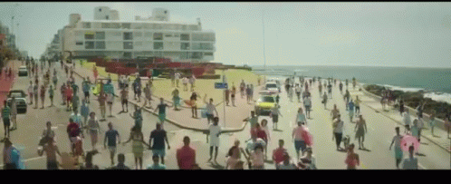 a crowd of people walk along a road by the ocean