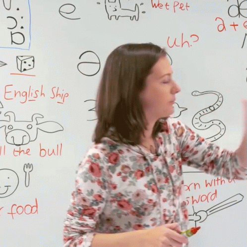 a woman with dark hair stands near a chalk board with drawings