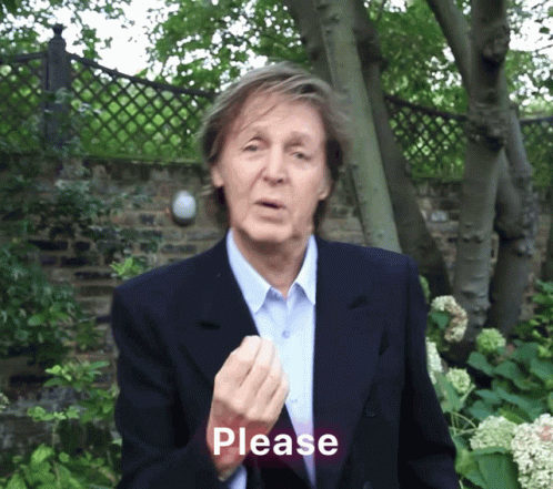 a man in a suit is standing near a fence and holding his hand up to his right with words that say please