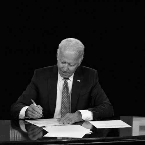 man in suit with tie writing on paper while sitting at desk