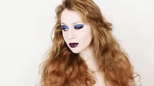a women with makeup and blue hair with white make up on her face
