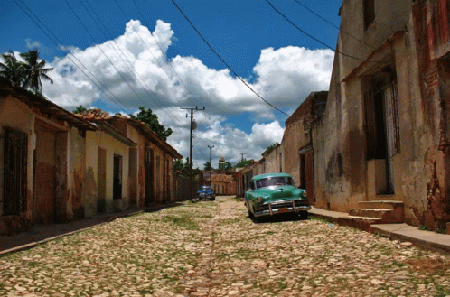 a street with blue gravel, a car on the far side, and a rusty orange sky in background