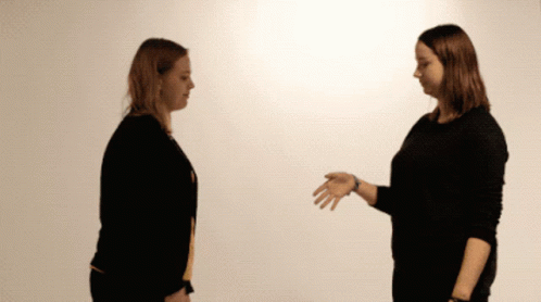 two women with black pants are talking in a white room