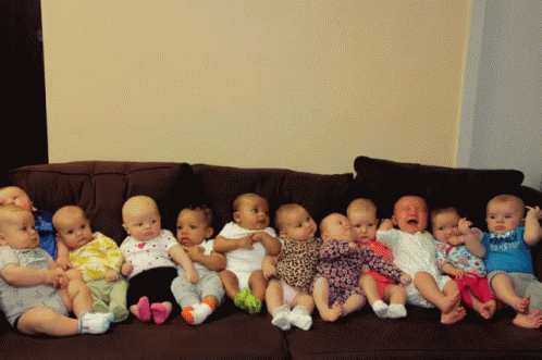 seven babies sit together on the couch looking at the camera