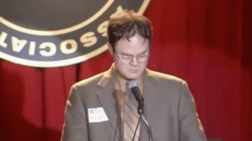 a man in a suit and glasses speaking at a microphone