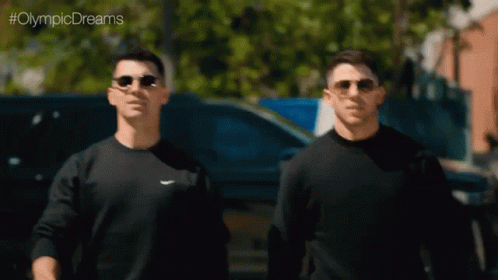 two men in sun glasses walk near each other