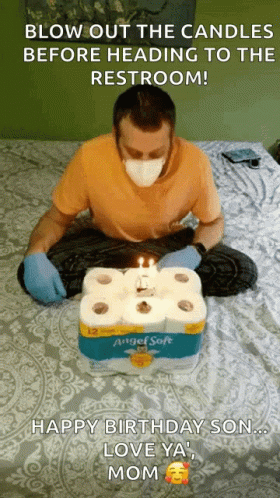 a man sitting on a bed blowing out the candles on his cake