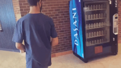 man looking at a small vending machine in front of brick wall
