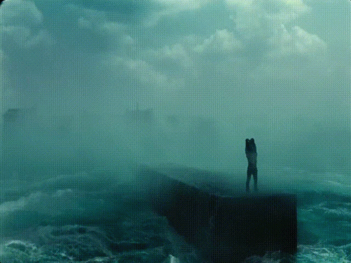 man standing on edge of cliff with green sea water