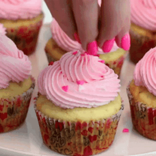 a close up of a person grabbing a frosted cupcake