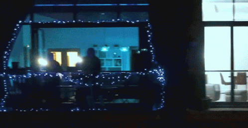 people walk outside in front of the window of a restaurant decorated with holiday lights