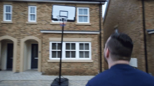 a man stands outside a blue house while playing basketball