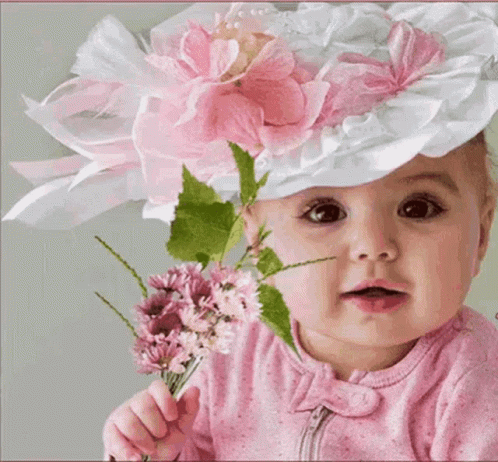 a blue - eyed baby holding up a flower, with other flowers