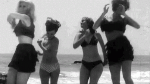 black and white po of three women in bathing suits by the beach
