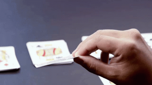 someones hand holding an unopened cigarette in front of some squares of cards