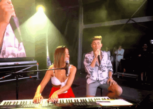 a young man and woman in front of keyboard instruments in front of music production lights