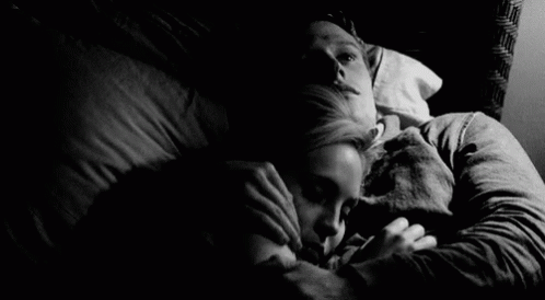 a woman lies in bed with a man as they cuddle next to her