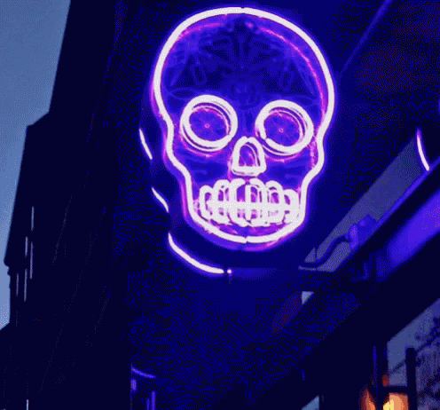 a neon skeleton sign hanging off the side of a building
